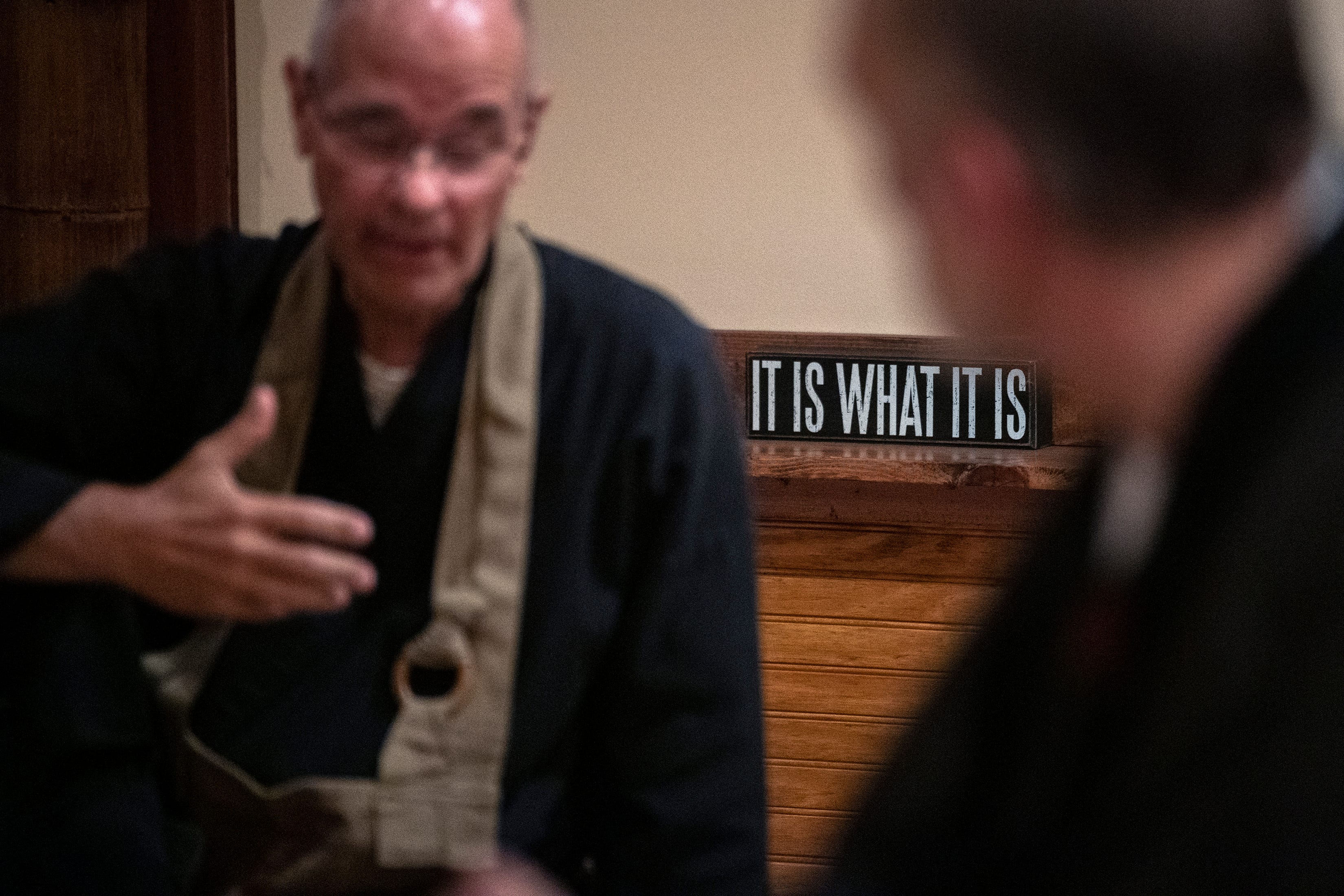 A sign reading 'It is what it is' is seen behind Zen Master Seijaku Roshi inside the zendo. Roshi was diagnosed with pancreatic cancer in April 2018. "He went through some terrible times and our hearts were so open. He’s taught us how to deal with suffering," said Chimon.
