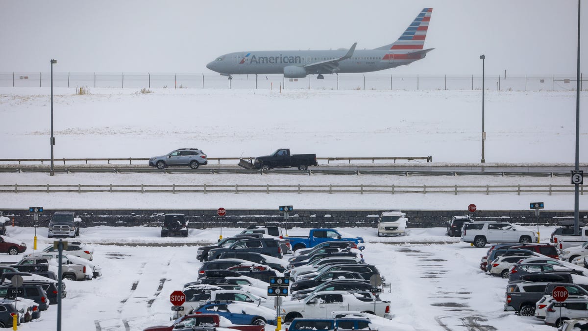 A jet passes snow-covered cars parked at Denver International Airport on Nov. 26, 2019, in Denver. Flights were delayed and rescheduled due to a winter storm that dropped nearly a foot of snow in the city. 