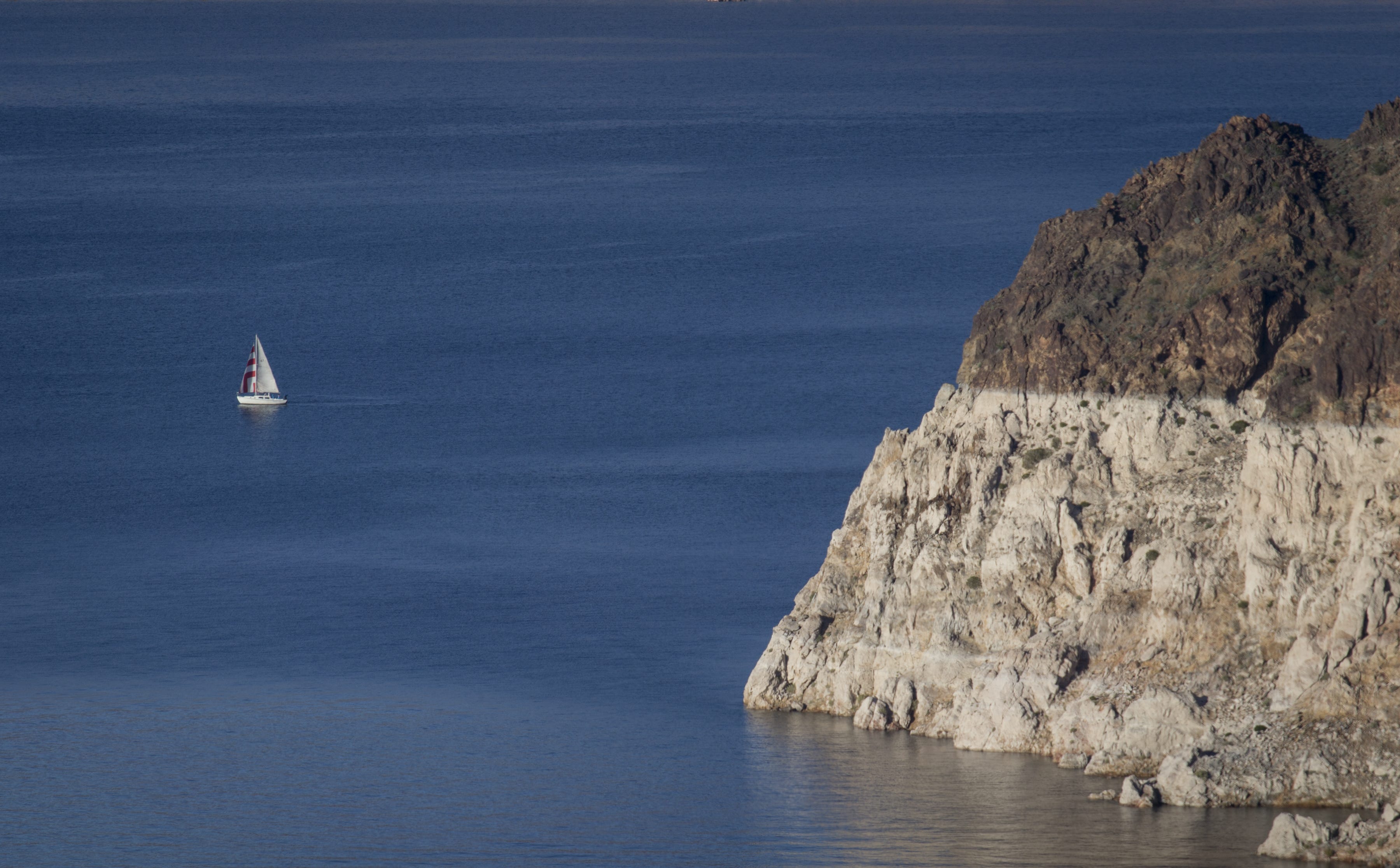 A sailboat cruises in the Lake Mead National Recreation Area near the Arizona-Nevada border. A high-water mark, or "bathtub ring," is visible on the shoreline.