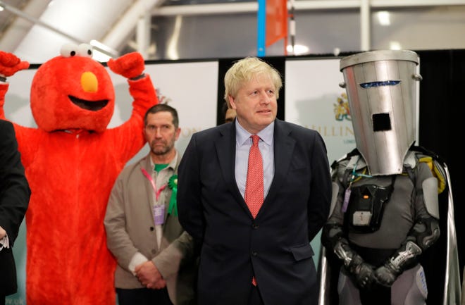 Bobby Smith, a political and fathers' rights activist and founder and leader of the "Give Me Back Elmo" party, left, and Independent candidate Count Binface, right, stand either side of Britain's Prime Minister Boris Johnson as they wait for the Uxbridge and South Ruislip constituency count declaration at Brunel University in Uxbridge, London, on Dec. 13, 2019.