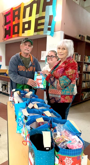 U. S. Marine Corps veteran Tim White receives a Christmas gift bag from Daughters of the American Revolution member Faith Morley at the Mesilla Valley Community of Hope. Kat McClure, center, is the  veteran services coordinator at the Community of Hope.