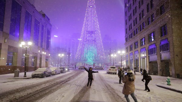 People pose for photos as snow falls in downtown I