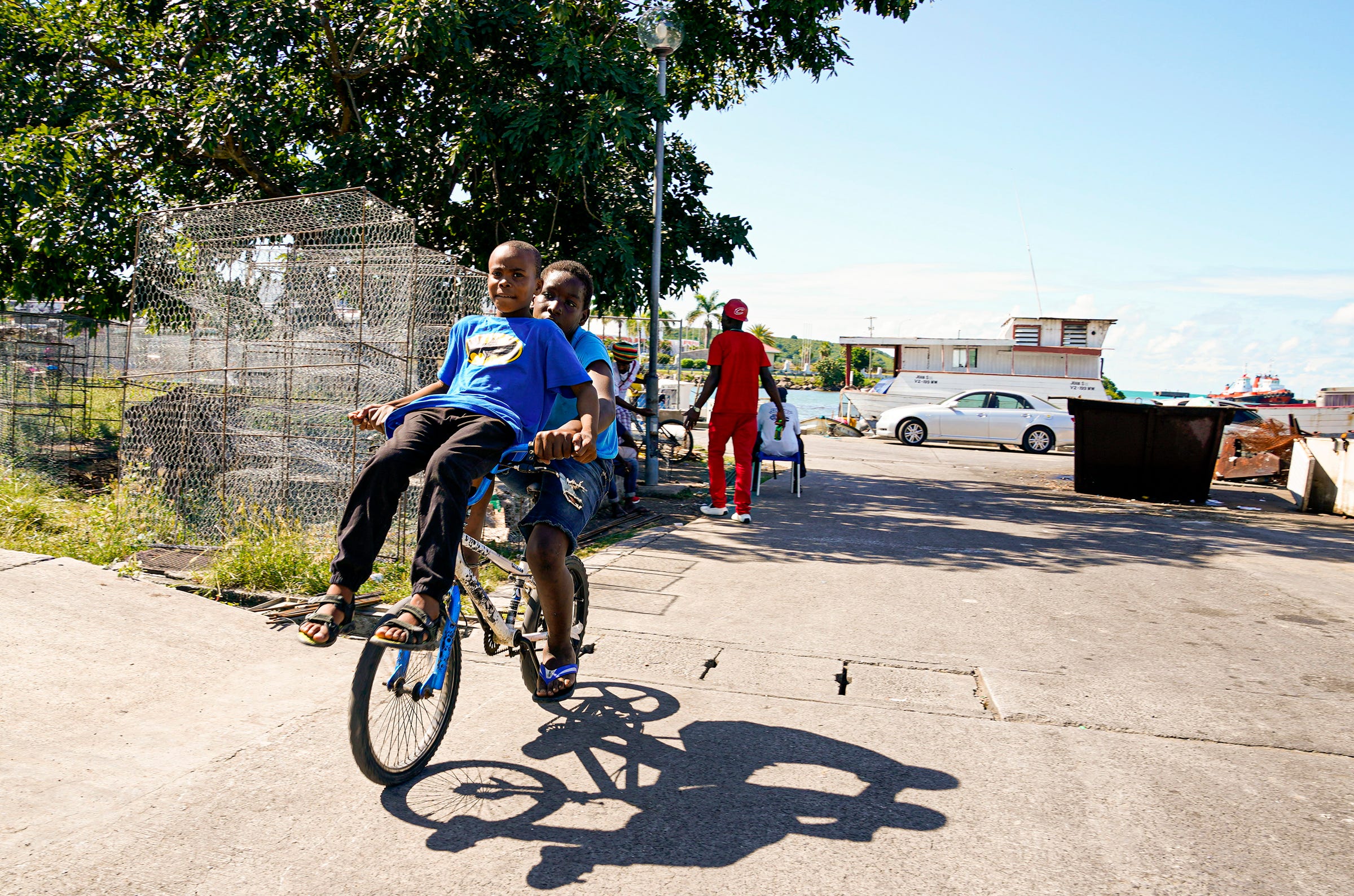 Two boys ride around the wharf in St. John's, the capital of Antigua. Local residents shop in the open air market along the busy streets of the city, buying vegetables and fruit, including pineapples, the official fruit of the country.