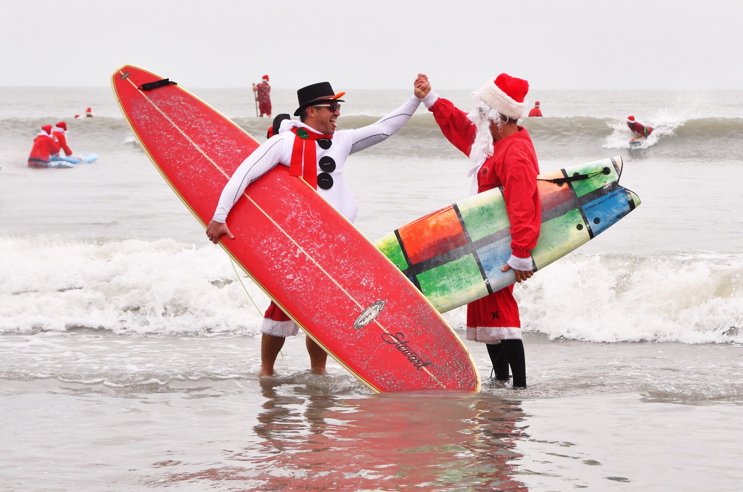 George Trosset Jr. and George Trosset, the two that started it all, high five each other. Thousands turned out to watch hundreds of Surfing Santas catch some waves in Cocoa Beach for the 10th annual Surfing Santas  event Tuesday morning. 10 years ago  George Trosset, his son George Jr. and his daughter-in-law went surfing in Santa and Christmas costumes behind their house on Christmas Eve.  The event has grown and now raises money for two local non profits - Grind for Life, which helps with financial assistance for cancer patients, and the Florida Surf Museum.