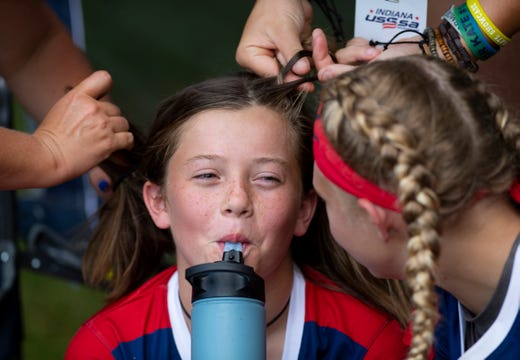 Peyton Pryor gets a double-team hair braiding by a team mom and her sister before the Midwest Astros South '07 softball team's first pool game at the Newburgh Softball Fields Wednesday afternoon, July 17, 2019.