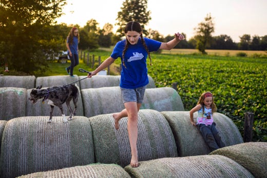 The sun sets at the Bennett household in Robards, Ky., as Madelyn, center, leads her dog Skye over hay bales while jumping around with her sisters Anna, back left, and Paige on the evening of Anna's 12th birthday, Thursday, July 25, 2019. When the weather is nice the sisters spend a majority of their free time playing outside. 