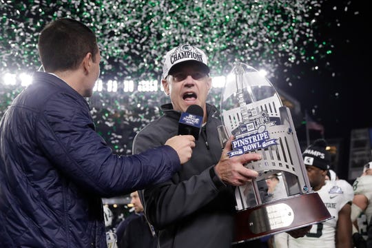 Michigan State head coach Mark Dantonio, right, speaks while holding the Pinstripe Bowl trophy.