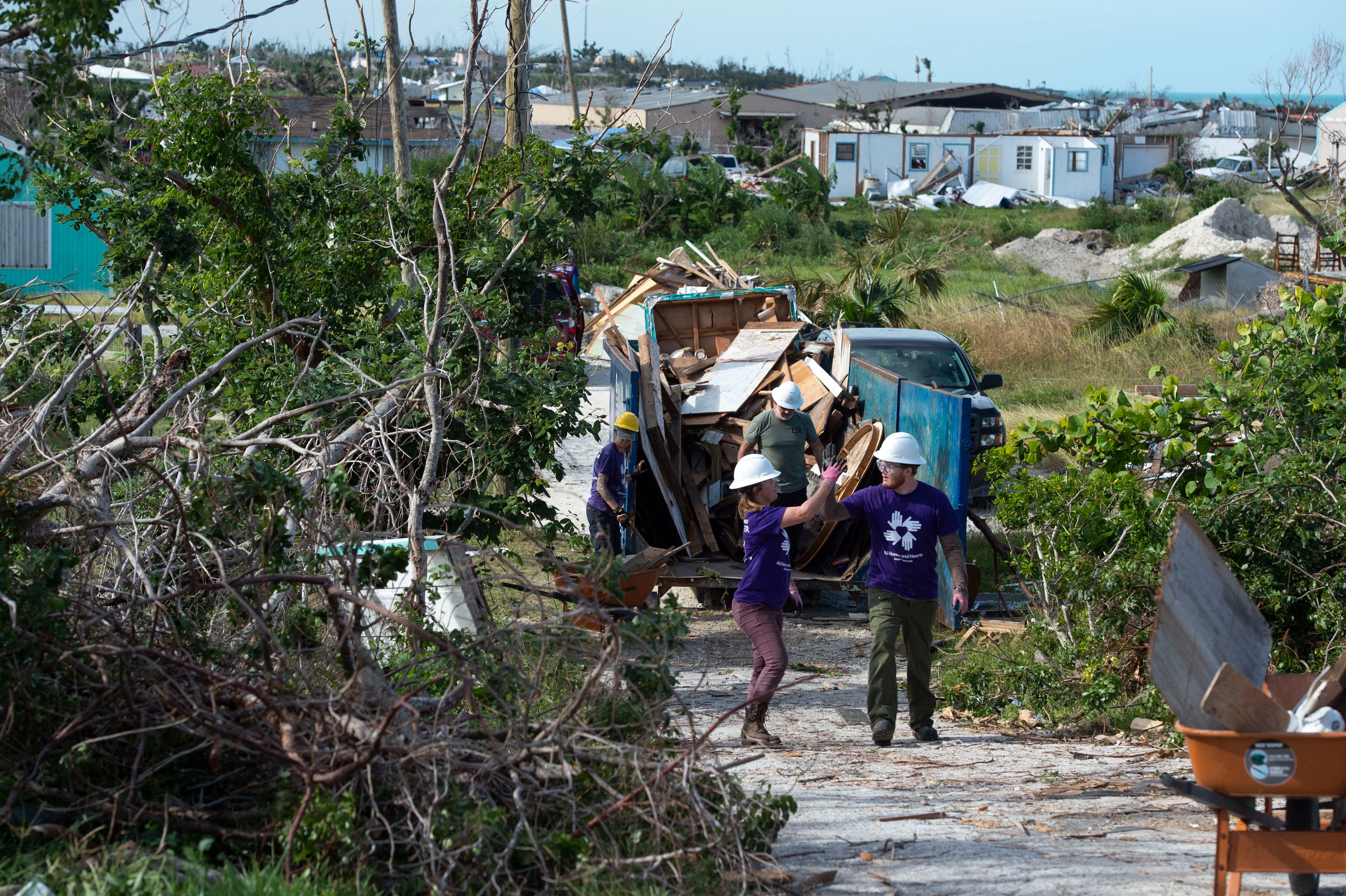 All Hands and Hearts Smart Response volunteers Corynn Benoit (left) and Ryan Ahlberg, both of Salt Lake City, Utah, high five as they remove debris scattered by Hurricane Dorian from a residential property Saturday, Dec. 21, 2019, in Marsh Harbour, Bahamas. The international nonprofit has worked alongside Vero Beach-based Youth on a Mission to clear debris, rebuild and roof homes and clean out moldy walls. 