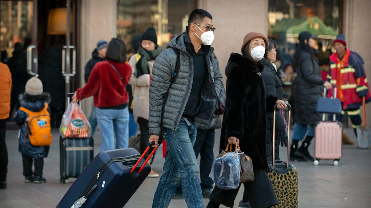 Travelers wear face masks as they walk outside of the Beijing Railway Station in Beijing, Monday, Jan. 20, 2020. China reported Monday a sharp rise in the number of people infected with a new coronavirus, including the first cases in the capital. The outbreak coincides with the country's busiest travel period, as millions board trains and planes for the Lunar New Year holidays.