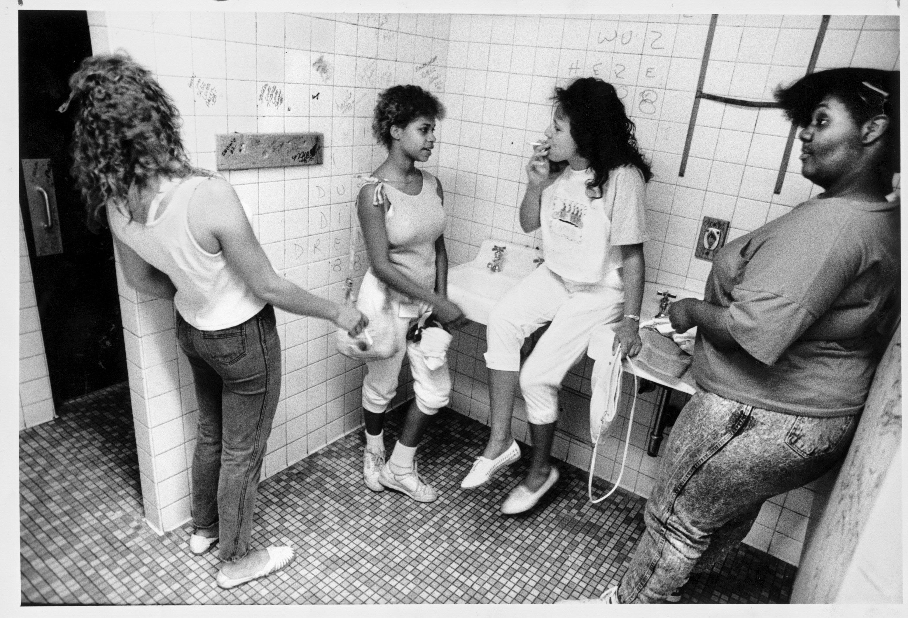 Tina Bussell watches for teachers or security guards while she and friends smoke in the girls lavatory.  The photo is a part of Manny Crisostomo's Pulitzer Prize-winning essay.  


