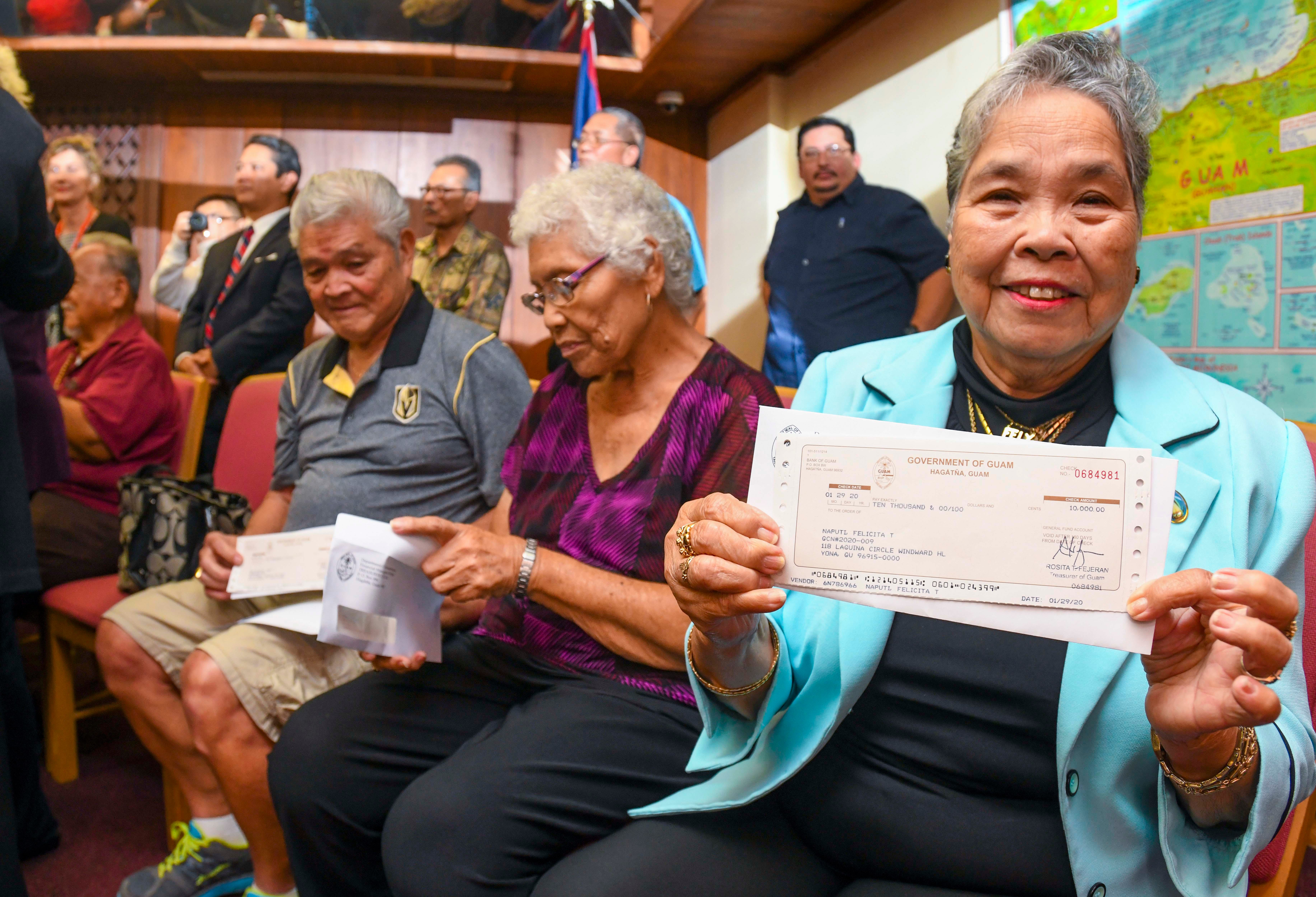 War claims recipient Felicita Naputi front, happily displays a check she received from Gov. Lou Leon Guerrero during a presentation at Adelup in this Jan. 29, 2020, file photo.