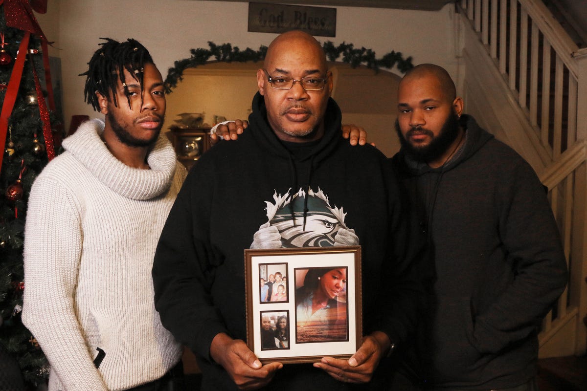 Leroy West holds a photo of his daughter, Robin West. He stands in his Philadelphia home, flanked by his sons and Robin's brothers, Azrien, 21, and Raymond, 27.