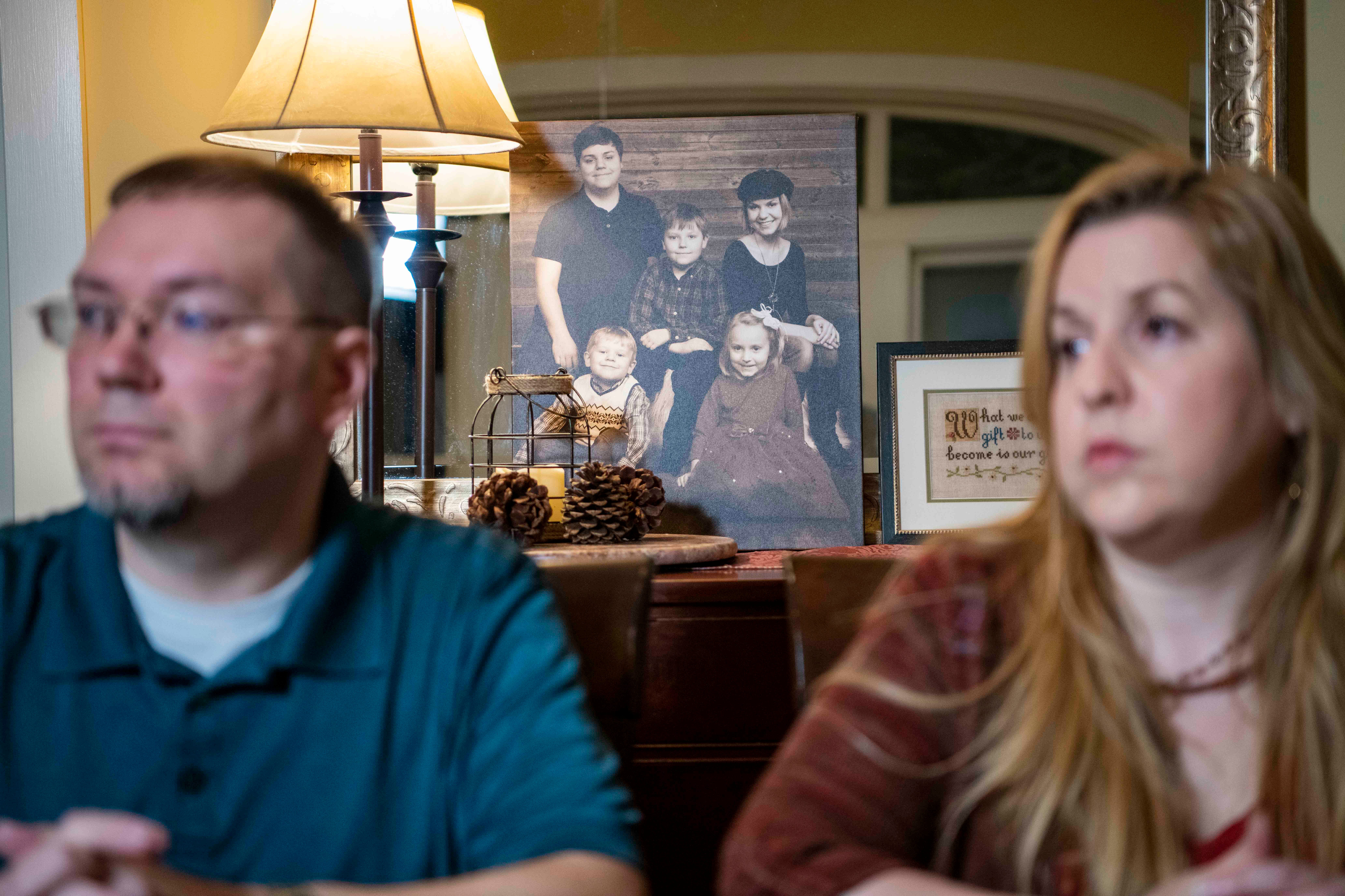 Dominique and Megan Benninger sit in front of a portrait of their five children in their home.