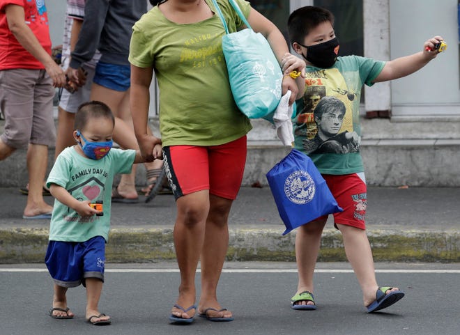 Children wearing protective masks cross a street in Mandaluyong, east of Manila, Philippines. The Philippines reported on Sunday, the first death of a new virus outside of China, where authorities delayed the opening of schools in the worst-hit province and tightened quarantine measures in another that allow only one family member to venture out to buy supplies. 