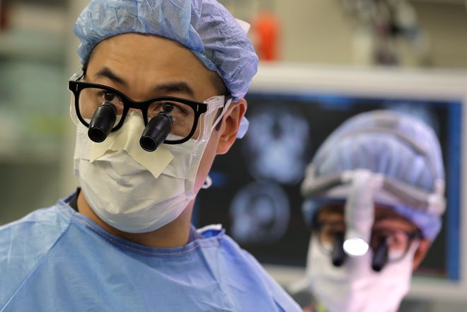 In this Jan. 14, 2020 photo, neurosurgeon Dr. Andrew Ko, left, of the University of Washington School of Medicine, wears glasses with magnifying lenses in the operating room as he works with senior resident Dr. Ariana Barkley, right, to perform brain surgery on Genette Hofmann at Harborview Medical Center in Seattle in hopes of reducing the epileptic seizures that had disrupted Hofmann's life for decades.
