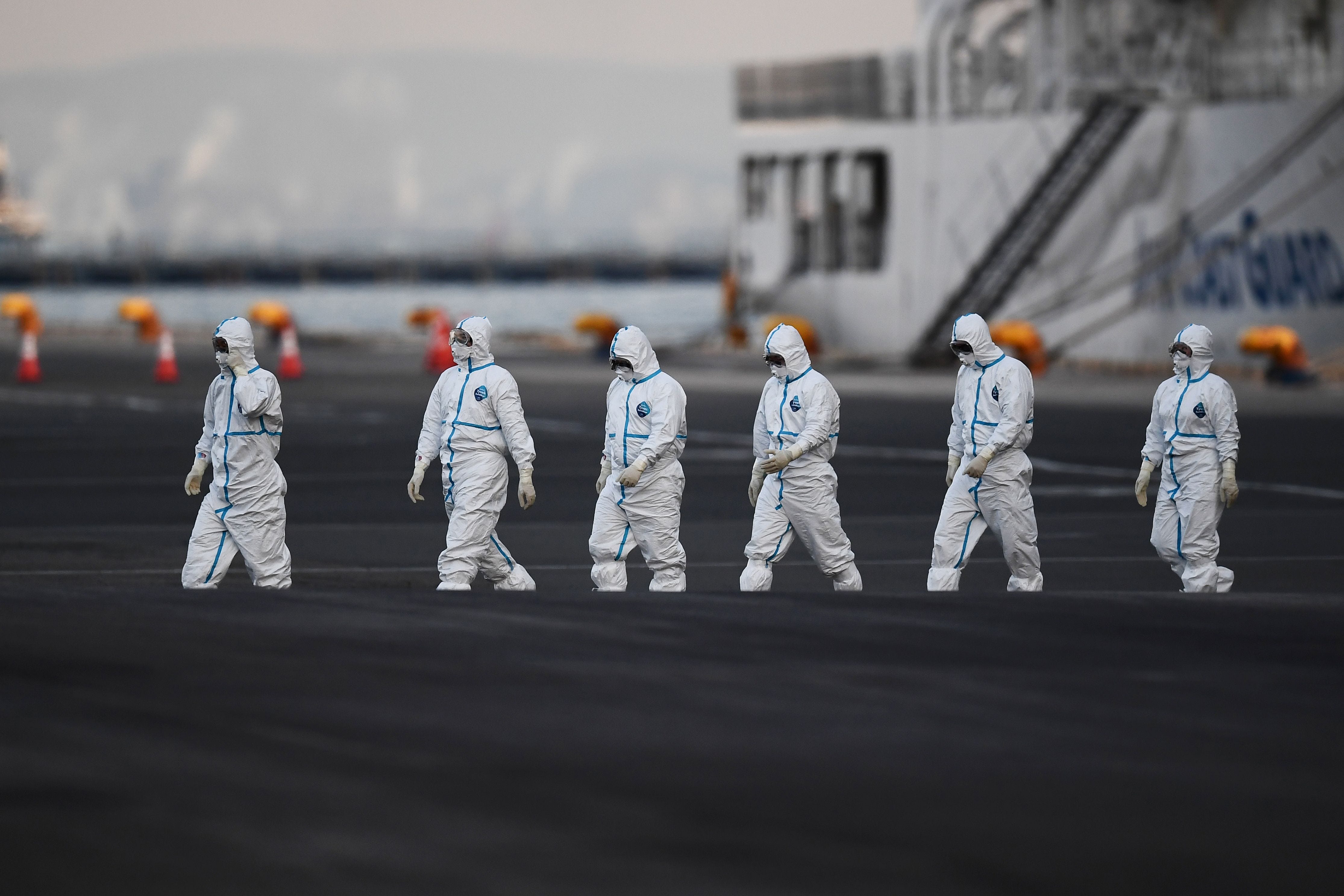 People wearing protective suits walk from the Diamond Princess cruise ship, with around 3,600 people quarantined onboard due to fears of the new coronavirus, at the Daikoku Pier Cruise Terminal in Yokohama port on Feb. 10, 2020. Around 60 more people on board the quarantined Diamond Princess cruise ship moored off Japan have been diagnosed with novel coronavirus, the country's national broadcaster said on February 10, raising the number of infected passengers and crew to around 130.