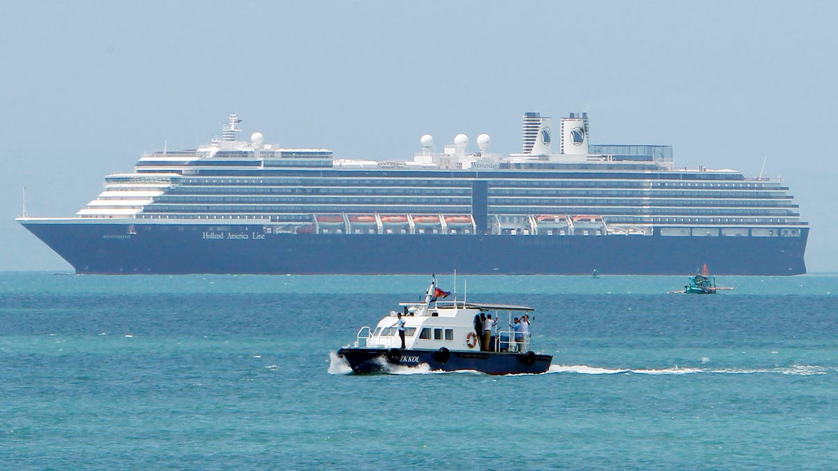 A speed boat, foreground, transports samples from some passengers who have reported stomachaches or fever, in the Westerdam, seen in the background, off Sihanoukville, Cambodia, Thursday, Feb. 13, 2020. The cruise ship turned away by four Asian and Pacific governments due to virus fears anchored Thursday off Cambodia for health checks on its 2,200 passengers and crew.