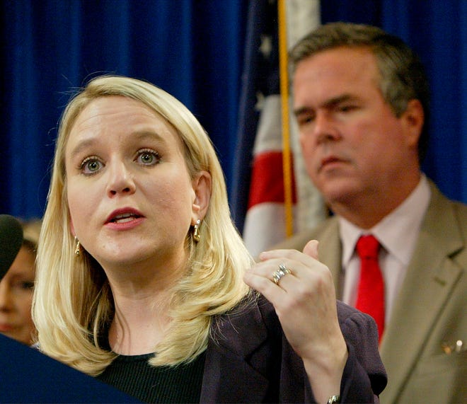 In this Tuesday, Sept. 28, 2004, file photo, Tiffany Carr, executive director of Florida Coalition Against Domestic Violence, left, speaks at a news conference held by Gov. Jeb Bush, background right, to announce a public awareness campaign designed to prevent disaster-related domestic violence, in Tallahassee, Fla. On Thursday, Feb. 13, 2020, Florida Gov. Ron DeSantis ordered an investigation into a nonprofit domestic abuse agency whose CEO, Carr, had received $7.5 million in compensation over a three-year span.