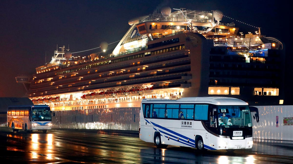 Buses carrying U.S. passengers who were aboard the quarantined cruise ship the Diamond Princess, seen in background, leaves Yokohama port, near Tokyo, early Feb. 17, 2020. The cruise ship was carrying nearly 3,500 passengers and crew members under quarantine.