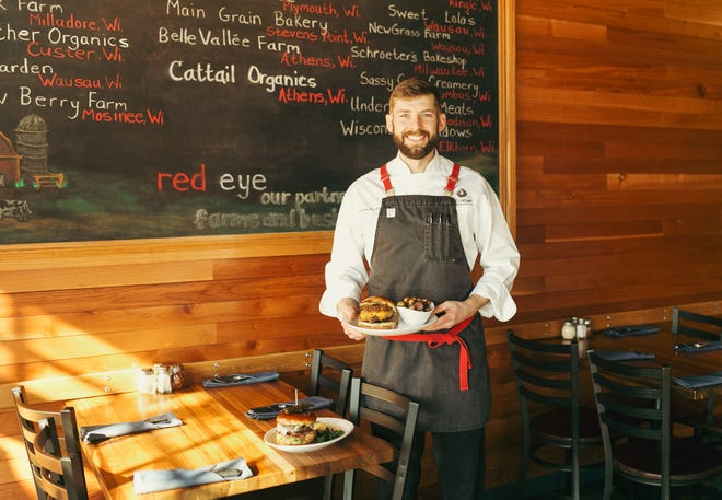 Executive Chef Nathan Bychinski of Red Eye Brewing Co. in Wausau holds their Wisconsin Burger made with pastured-raised, grass-fed local beef topped with a six-year cheddar from Carr Valley Cheese. The Wisconsin Burger is a personal favorite of Bychinski’s along with their Red Eye Sancho Burger on the table.