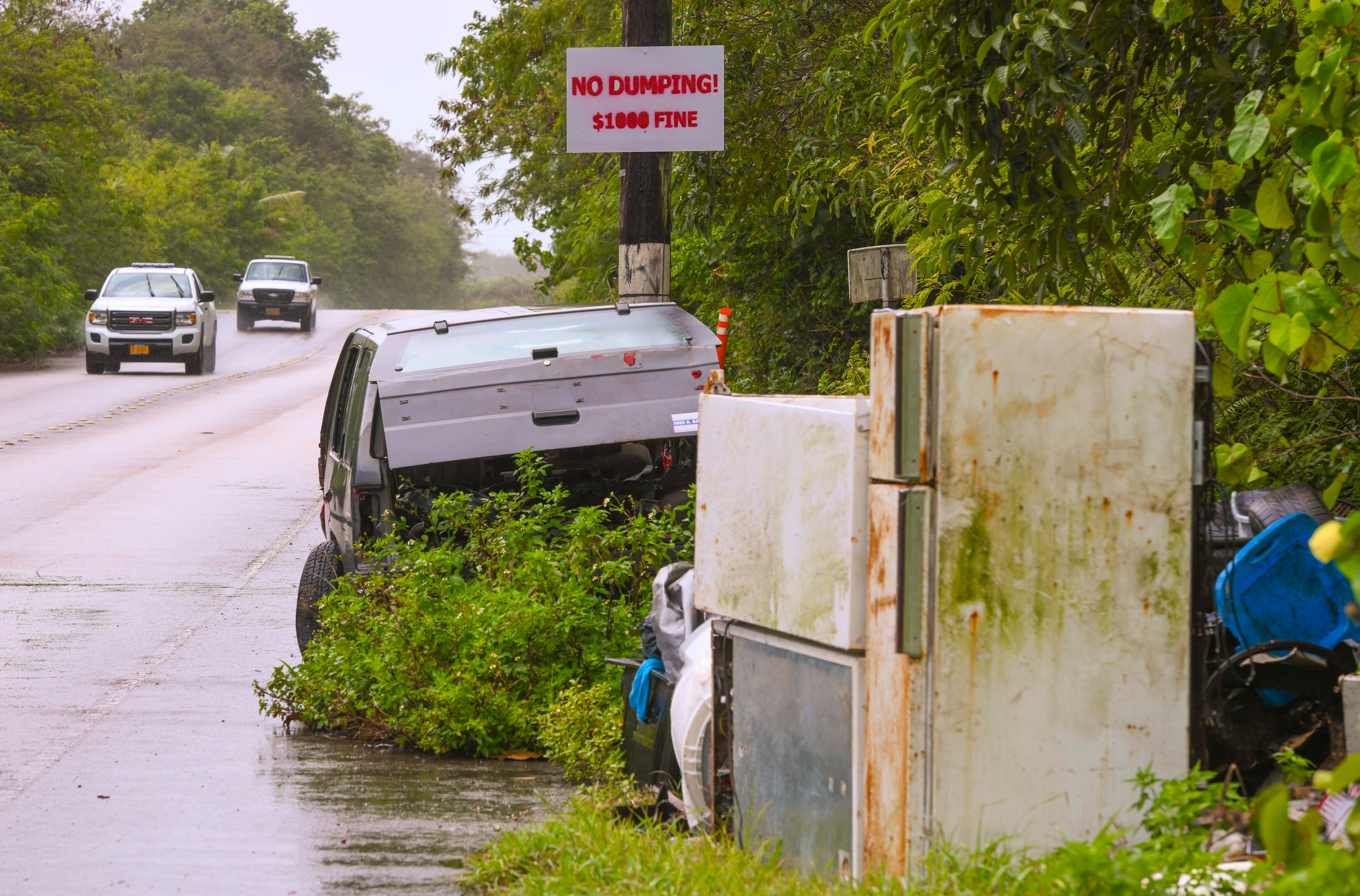An abandoned vehicle, appliances and other discarded debris seen at the base of a utility pole with a sign, stipulating the penalty for illegal dumping, along Bumuchachu Street in Dededo in this Feb. 25 file photo.