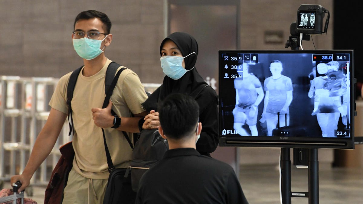 A couple, wearing protective facemasks amid fears about the spread of the COVID-19 novel coronavirus, walk past a temperature screening check at Changi International Airport in Singapore on Feb. 27, 2020. 