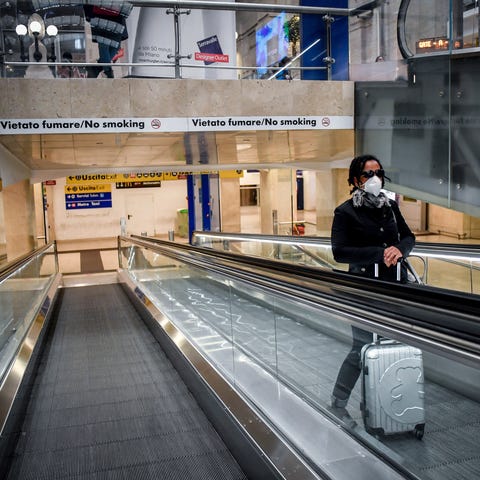 A woman wears a mask as she stands on an escalator