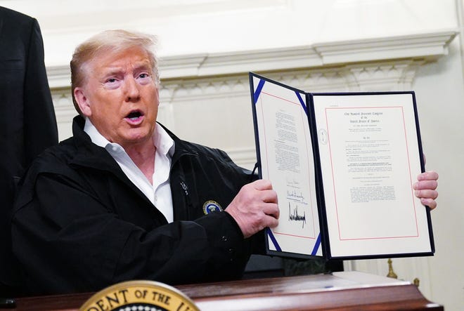 US President Donald Trump holds up an USD 8 billion emergency funding bill to combat COVID-19, coronavirus, after signing it in the Diplomatic Room of the White House in Washington, DC on March 6, 2020. (Mandel Ngan/AFP via Getty Images/TNS)