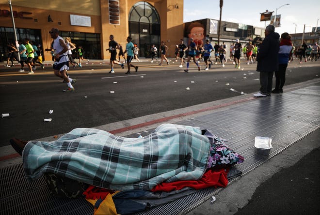 A homeless person sleeps as runners jog past during the Los Angeles Marathon, which was allowed to continue by health officials in spite of coronavirus COVID-19 fears, on March 8