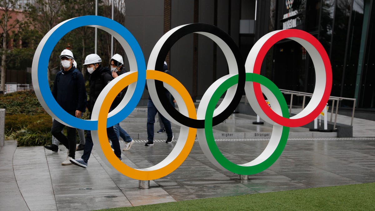 People wearing masks walk past the Olympic rings near the New National Stadium in Tokyo.