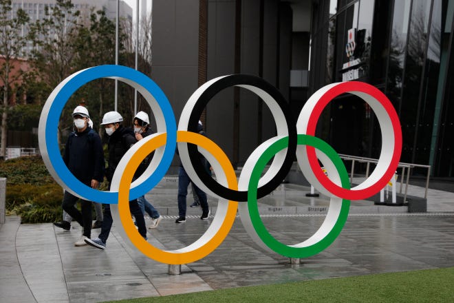 People wearing masks walk past the Olympic rings near the New National Stadium in Tokyo.