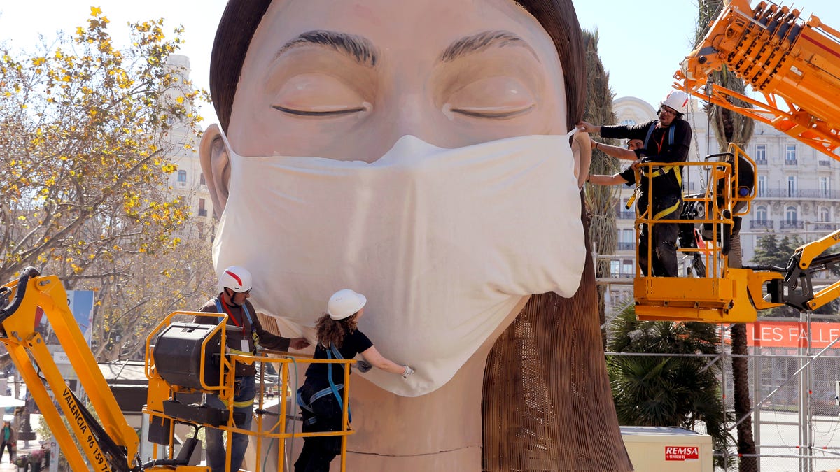 Workers place a mask on the figure of the Fallas festival in Valencia, March 11, 2020. The Fallas festival which was due to take place on March 13 has been cancelled over the coronavirus outbreak. For most people, the new coronavirus causes only mild or moderate symptoms, such as fever and cough. For some, especially older adults and people with existing health problems, it can cause more severe illness, including pneumonia.