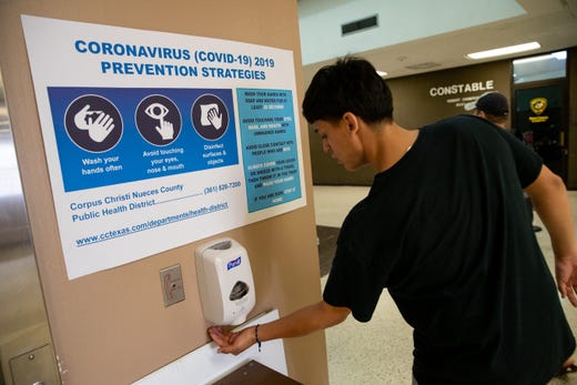 A man uses hand sanitizer underneath a coronavirus prevention sign at the entrance of the Nueces County Courthouse on Friday, March 13, 2020.