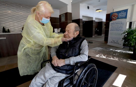 With gloves, mask and gown on, Johanna Mannone, 79, caresses her husband, Mike, in the front room of WellBridge of Rochester Hills on Friday. Johanna was given onetime, special permission to see her husband, who has been in the facility after suffering two strokes. She doesn't know when she'd get to see him again.