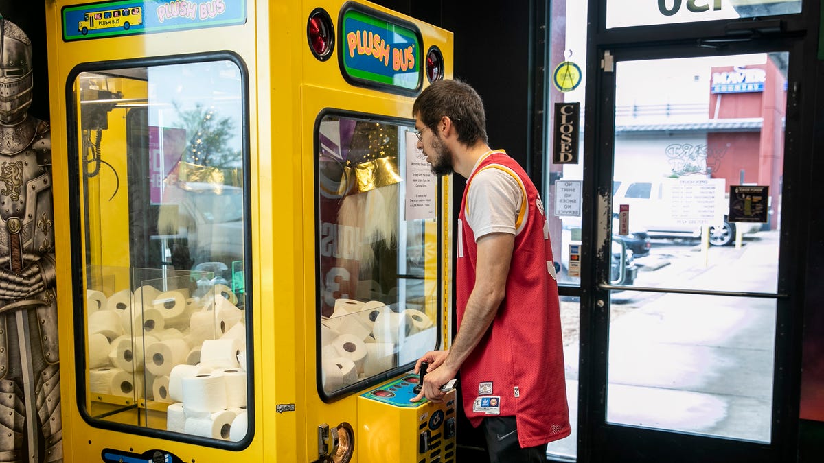 Jose Medellin tries his luck winning a roll of toilet paper from a claw machine arcade game at Wizard Hat Smoke Shop in Pflugerville, Texas, on Sunday March 15, 2020.  The arcade game was filled with rolls of toilet paper as a lighthearted reaction to the toilet paper shortage caused by the coronavirus outbreak.