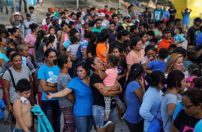 In this Aug. 30, 2019, file photo, migrants, many who were returned to Mexico under the Trump administration's "Remain in Mexico," program wait in line to get a meal in an encampment near the Gateway International Bridge in Matamoros.