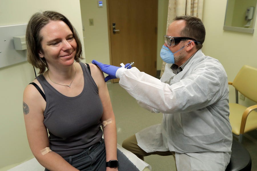 Jennifer Haller, left, smiles as the needle is withdrawn after she was given the first-stage safety study clinical trial of the potential vaccine.