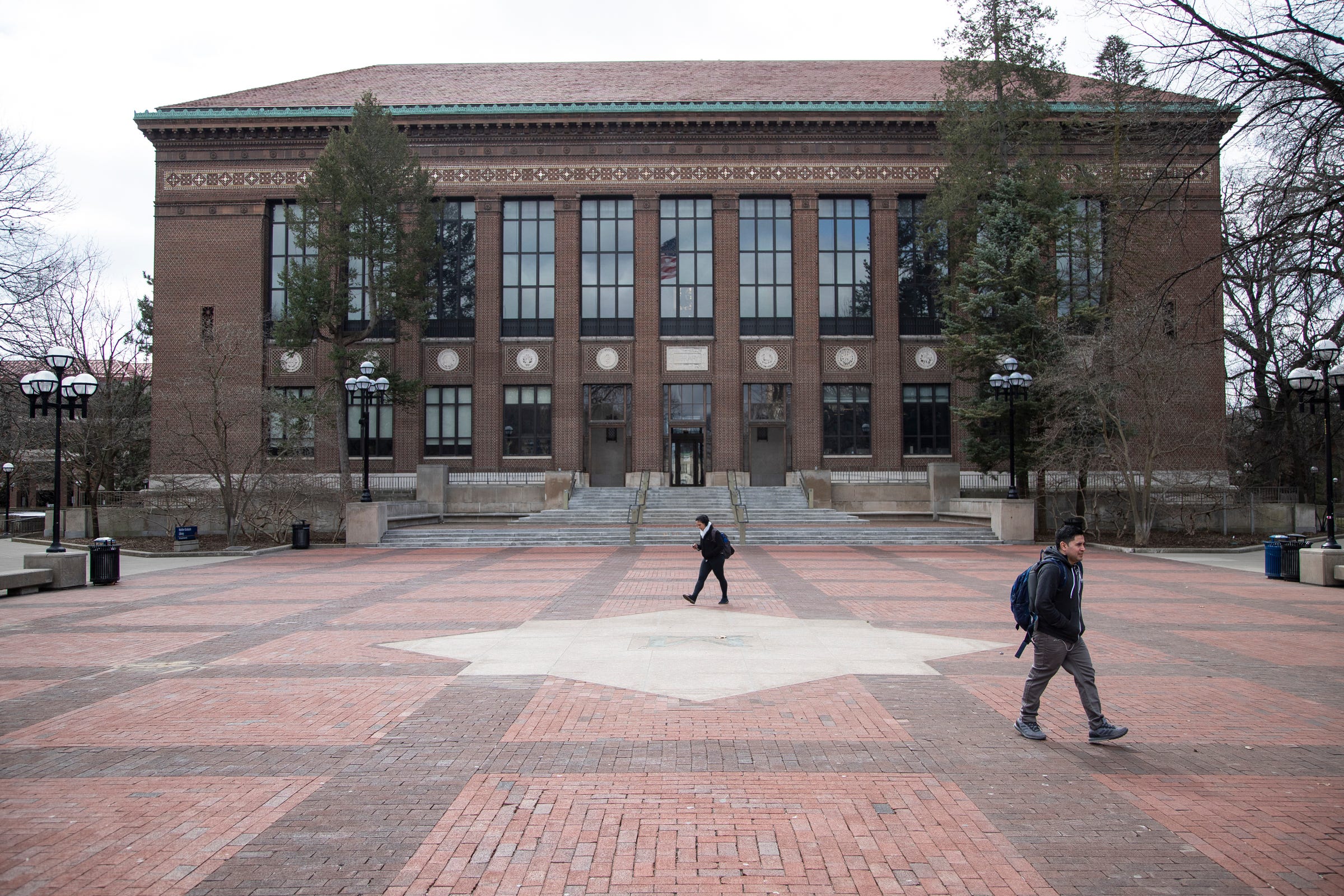 People walk across the Diag in front of Hatcher Graduate Library on University of Michigan's  main campus in Ann Arbor, Tuesday, March 17, 2020.