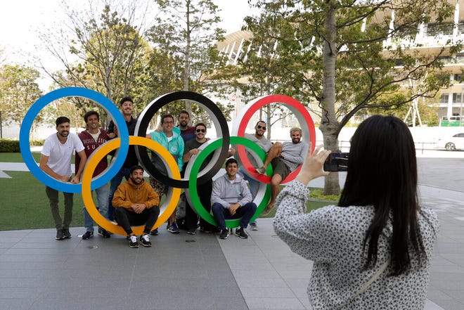 A group of students from Uruguay pose for a souvenir picture on the Olympic Rings set outside the Olympic Stadium in Tokyo, Saturday, March 21, 2020. The Olympic flame from Greece arrived in Japan Friday, even as the opening of the the Tokyo Games in four months is in doubt with more voices suggesting the games should to be postponed or canceled because of the worldwide virus pandemic. (AP Photo/Gregorio Borgia)