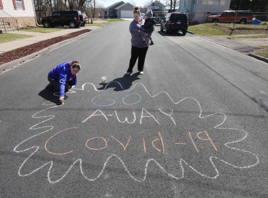 Laura Ryan does a chalk art message on March 21, 2020 in Swoyersville, Pa. as neighbor Lindsey Stewart watches with her son Seth, 2.