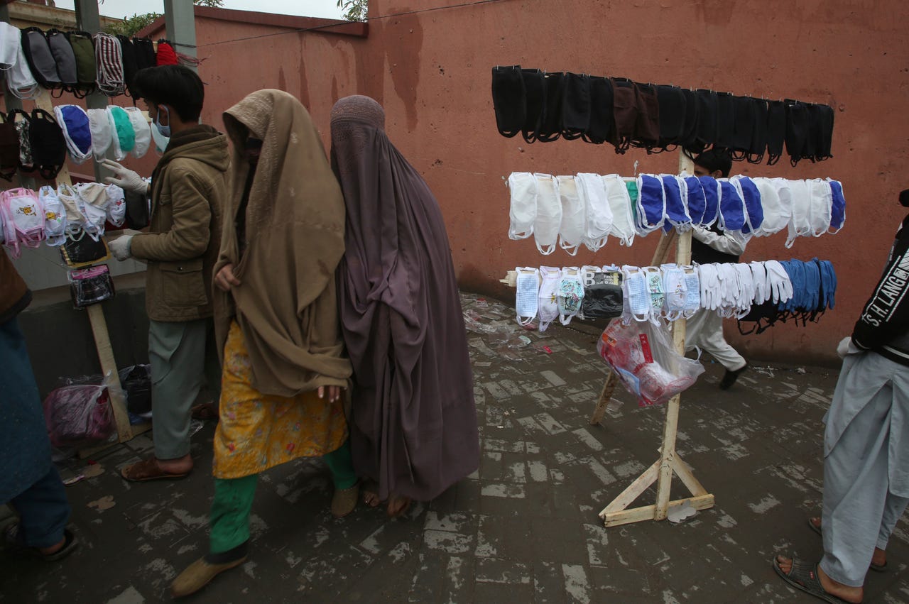 Pakistani women walk past vendors selling face masks to prevent the spread of the coronavirus, in Peshawar, Pakistan, March 24, 2020. Pakistani authorities said they'd shut down train operations across the country from Wednesday until March 31 in an effort to contain the spread of the virus.