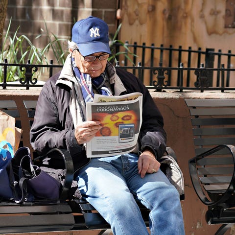 A man in New York sits on a bench reading a newspa