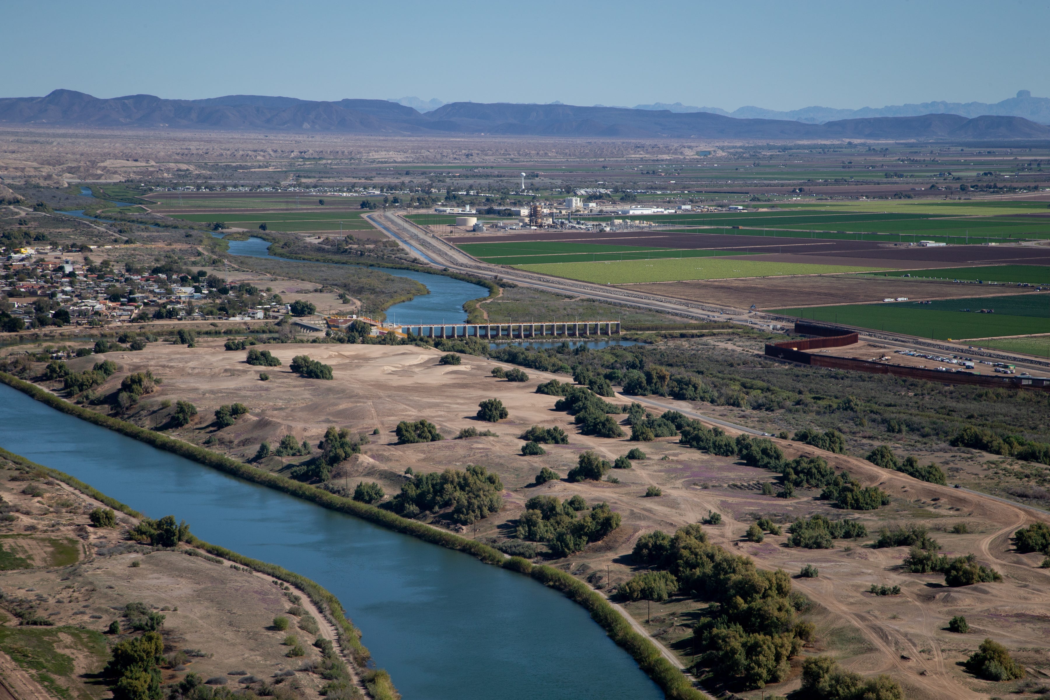 The Colorado River (top center) flows up to Morelos Dam on the U.S.-Mexico border. The Colorado River channel continues next to the border wall (right center), while the Reforma Canal (lower left) carries water to farms and cities in the Mexicali Valley.