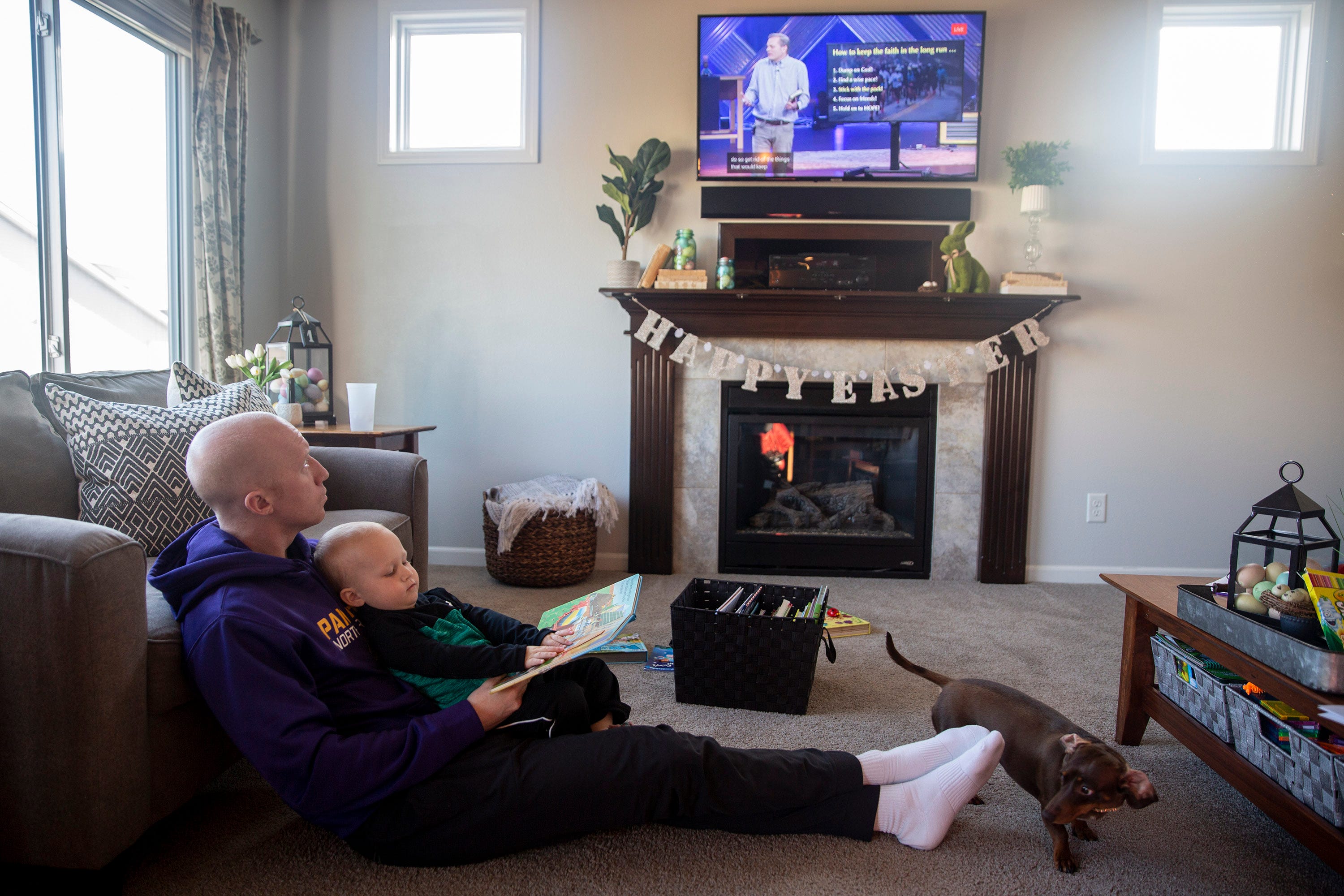 Matthew Burch watches a livestream of one of Lutheran Church of Hope's Sunday morning services with his two-year-old son, Hudson, and dog, Ruby, while sitting on the living room floor Sunday, March 29, 2020, in the family's home in Waukee. The Burches have been connecting with their church through these livestreams since the spread of COVID-19 canceled in-person services.