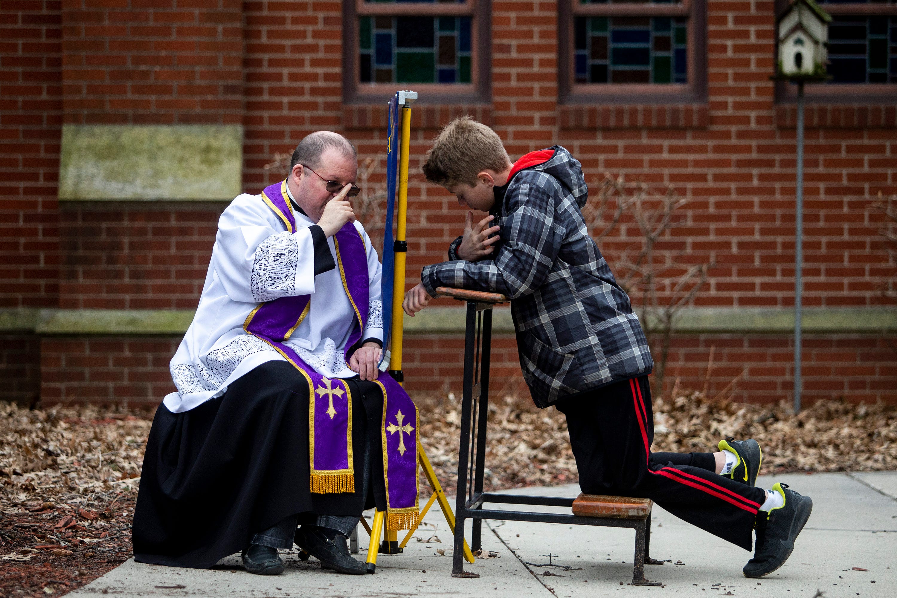 The Rev. P.J. McManus, of Christ the King Church, gives a blessing while hearing confession from Johnny, a parishioner of Christ the King, outside of the church's entrance on Tuesday, March 24, 2020, in Des Moines. McManus moved confession outside after the rise of COVID-19 in Iowa.