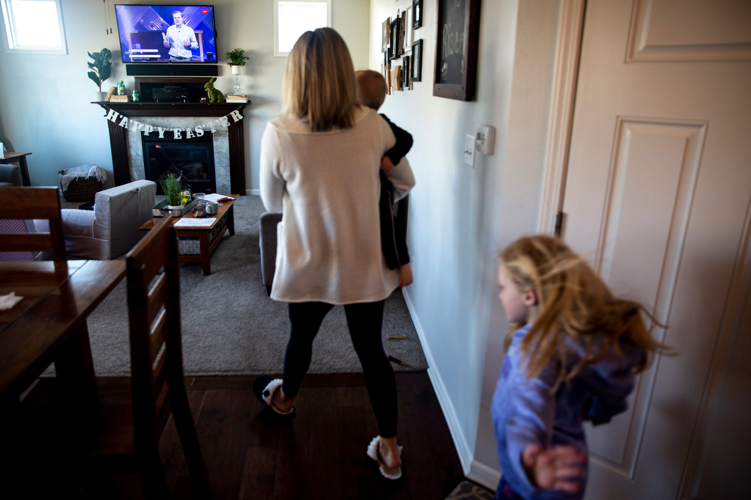 Asheley Burch carries her son, Hudson, while her daughter, Harper, follows, back to their living room to watch the livestream of Lutheran Church of Hope's Sunday morning service on March 29, 2020, from the family's home in Waukee. Themed coloring pages, books and games were used to keep the kids entertained during the service.