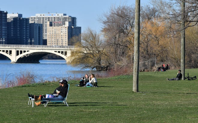 From left, Demeeka Lewis, 40, of Southfield and Queda McDaniel, 41, of Detroit relax in lounge chairs while they and others enjoy the sunshine in the evening, staying a safe distance apart, on Belle Isle in Detroit on April 2, 2020.