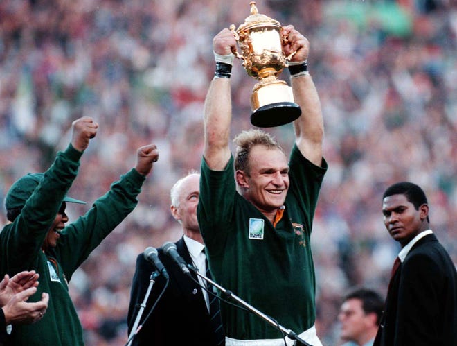In this June 24, 1995, file photo, South African rugby captain Francios Pienaar, center, raises the trophy after receiving it from South African President Nelson Mandela, left, who wears a South African rugby shirt, after they defeated New Zealand in the final 15-12 at Ellis Park, Johannesburg. Mandela strode onto the field wearing South African colors and bringing the overwhelmingly white crowd of more than 60,000 to its feet. They chanted "Nelson! Nelson! Nelson!" as Mandela congratulated the victorious home team in a moment that symbolized racial reconciliation.