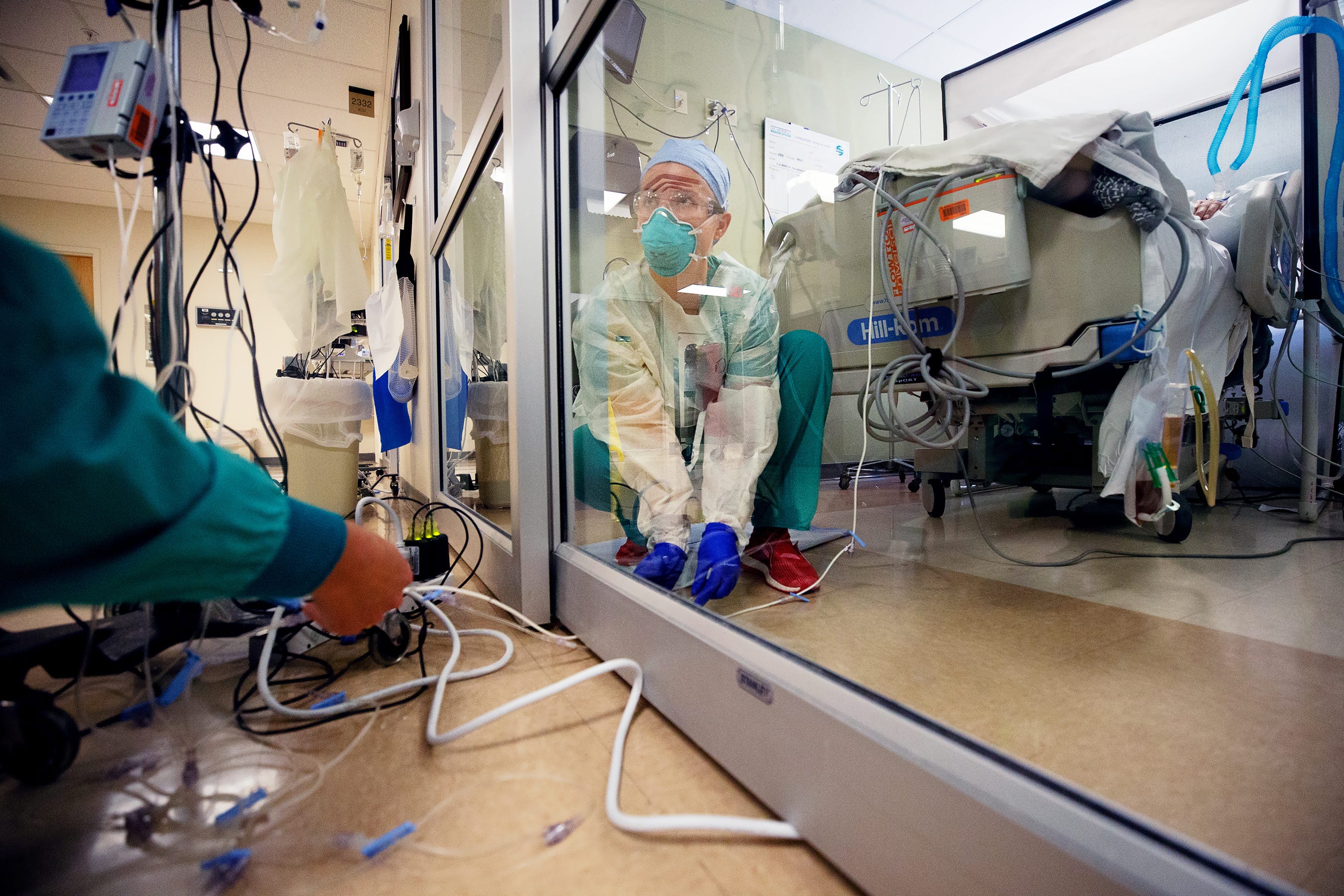 Monitoring equipment cords from outside a COVID-19 patient's room are pushed under the door to Registered Nurse Aubry Sander in the intensive care unit at Gulf Coast Medical Center in Fort Myers, Fla. This is done to reduce the number of times a patient's door is opened and helps prevent cross-contamination.