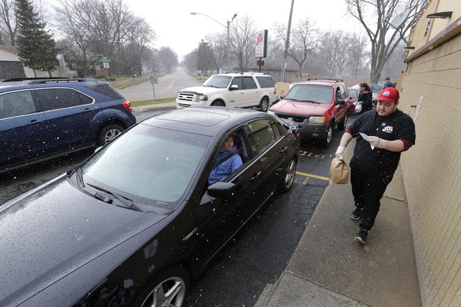Angel Reyes delivers a drive up lunch order to Dave McCracken at JD's Drive-In on Thursday in Appleton in the midst of snow flurries. Vehicles were lined up around the entire restaurant waiting to order.